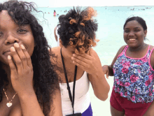 two women covering their faces with their hands while standing on the beach