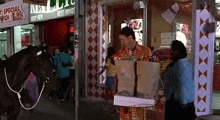 a man is riding a horse in front of a store while a woman pushes a shopping cart .