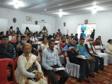 a group of people sit in a room with a sign on the wall that says ' ashir '