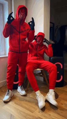 two men in red hoodies and masks pose for a photo