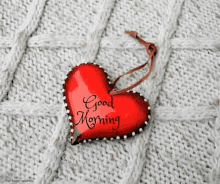 a red heart with the words `` good morning '' written on it is hanging on a knitted blanket .