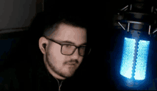 a man wearing glasses and ear buds is sitting in front of a blue light