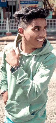 a young man wearing a green hoodie and a watch is smiling