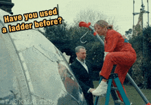 a woman in a red jumpsuit is sitting on a ladder while a man in a suit stands behind her