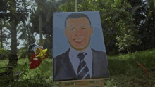 a painting of a man in a suit and tie is on a wooden easel in the grass .