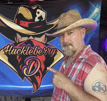 a man wearing a cowboy hat points to his tattoo in front of a huckleberry d. banner