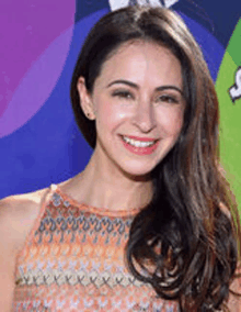 a woman with long hair is smiling for the camera while standing on a red carpet .