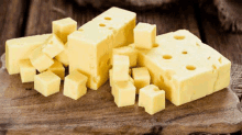 a wooden cutting board topped with slices of cheese and cubes of cheese .