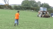 a young boy is running in a field with a tractor behind him .