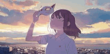 a girl is holding a cat mask over her face in front of a city .