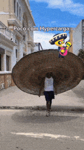 a man wearing a sombrero is walking down a street with a poco com hypercarga sticker on his hat