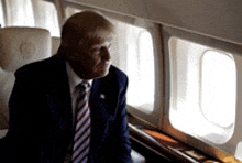 donald trump is sitting on an airplane and looking out the window .