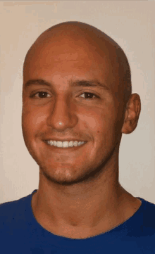 a bald man wearing a blue shirt smiles at the camera