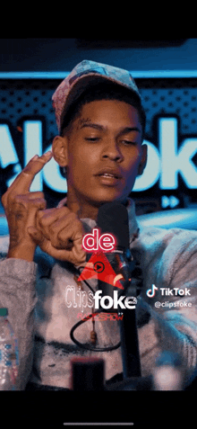 a young man is giving the middle finger in front of a microphone while a tiktok video is playing behind him .