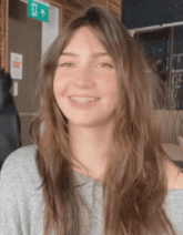 a girl with braces smiles in front of a green exit sign