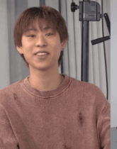 a young man wearing a pink sweater is smiling in front of a camera