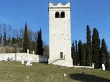 a white tower is sitting on top of a grassy hill surrounded by trees .