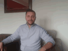 a man is sitting on a couch in a living room and smiling for the camera .