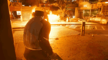 a man is standing in front of a burning building with a police car in the background