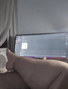 a person is laying on a bed in front of a computer monitor .