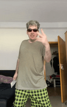 a man wearing sunglasses and plaid pants is giving a peace sign