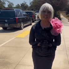 a woman in a black dress with a pink flower on her shoulder is standing in front of a black cadillac