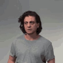 a man with long hair is wearing a gray t-shirt and looking at the camera .