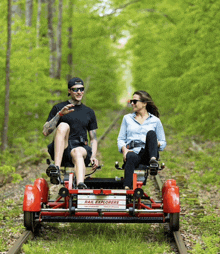 a man and a woman are riding a red rail explorer