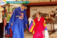 a man in a blue robe stands next to a woman in a red dress in front of a sign that says lang van hoa dan gia