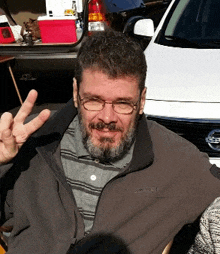 a man giving a peace sign in front of a white nissan car