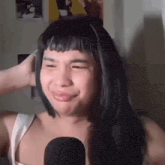 a woman with long black hair and bangs is making a funny face while standing in front of a microphone .