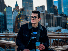 a man wearing sunglasses and a black jacket holds a cup of coffee