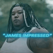 a man with dreadlocks and a white tank top is standing in front of a sign that says " james impressed "