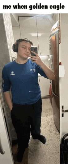 a man is taking a selfie in front of a mirror while wearing headphones and a blue shirt .