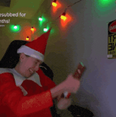 a person wearing a santa hat is sitting in front of a sign that says ' esubbed for months '