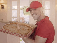 a man in a red hat is holding a pizza in a box