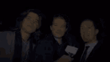 a group of three men standing next to each other in a dark room . one of the men is holding a microphone .