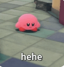 a pink kirby doll is sitting on a tiled floor with the words " hehe " written below it .