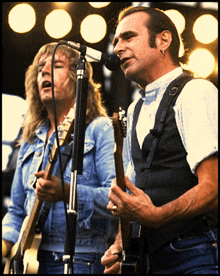 two men playing guitars and singing into microphones