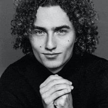 a black and white photo of a young man with curly hair and a black shirt .