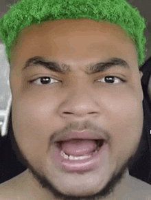 a man with green hair is making a funny face with his mouth open .