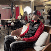 a man is sitting in a chair looking at his phone and wearing a hat that says ' alonso ' on it