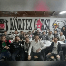 a group of men posing for a picture in front of a korfez carsi banner