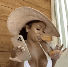 a woman in a bikini is holding a cell phone and drinking from a straw .