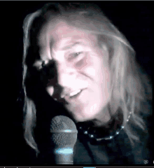 a man with long blonde hair is singing into a microphone in the dark