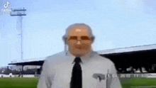 a man wearing a tie and sunglasses is standing in front of a soccer field .