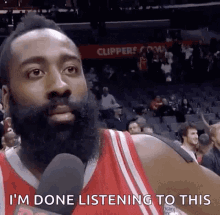 a basketball player with a beard is talking into a microphone while sitting in the stands at a game .