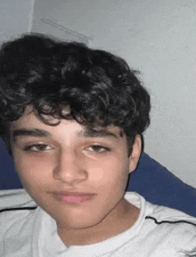 a young man with curly hair is taking a selfie while sitting on a bed .