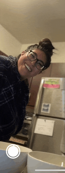 a woman with glasses is smiling in front of a refrigerator