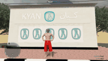 a man in red shorts is standing in front of a large sign that says kyan